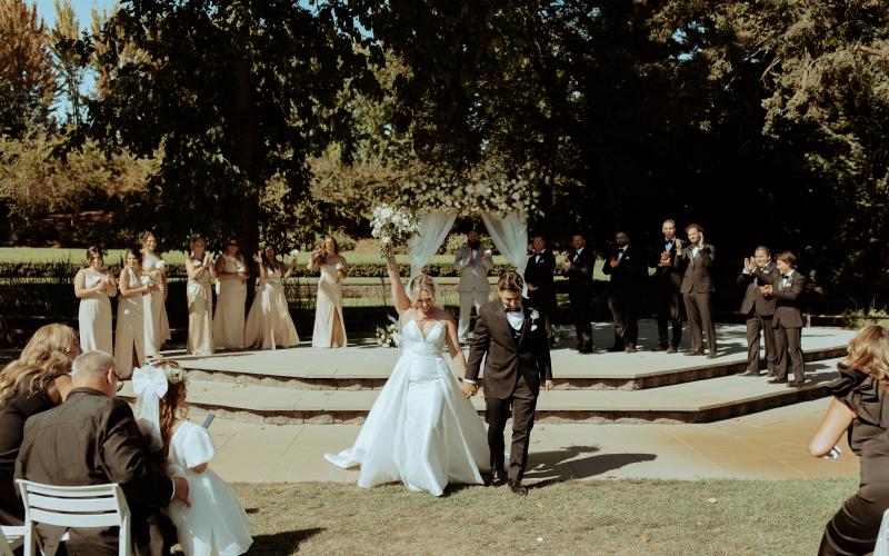 couple cheering and walking down aisle, ceremony arbor in background